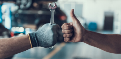 One hand holding a wrench and another giving a thumbs-up.