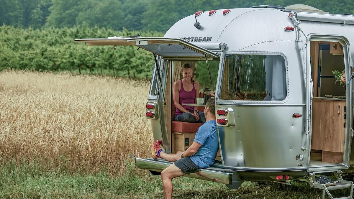 A young couple sitting in the back of their Airstream trailer