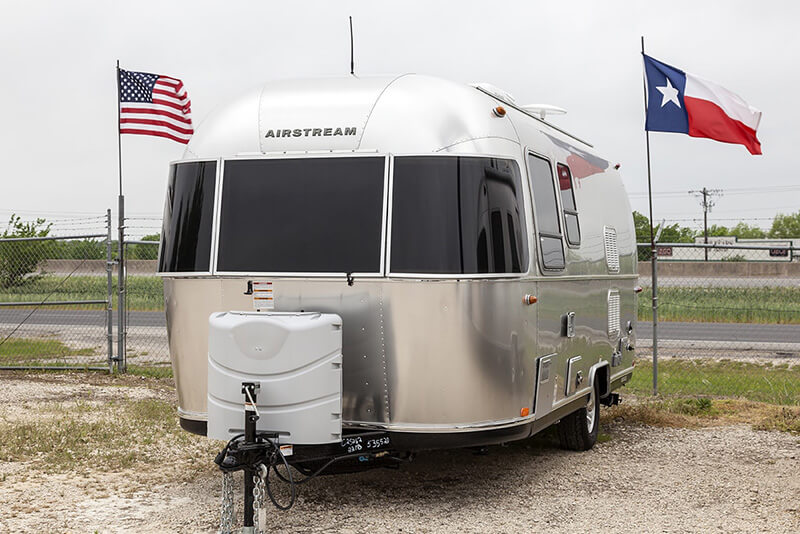 Airstream sitting in between a United States flag and a Texas flag.