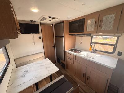 Modern kitchen with 2-burner stovetop, microwave, and refrigerator in used 2022 Prime Time RV Avenger 16FQ