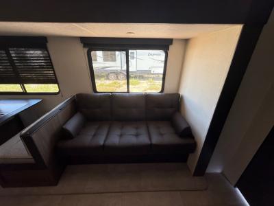 Living area slide of new 2026 Prime Time Tracer 295DB contains a jack knife sofa and booth dinette