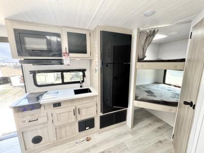 Kitchen microwave, glass-topped stovetop, and refrigerator next to double bunks in new 2026 East to West Della Terra 191BH RV