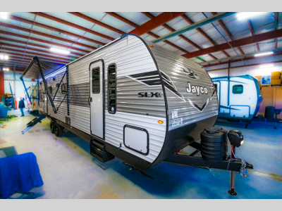 Front exterior of the 2025 Jay Flight SLX 330TBS with propane tanks, power tongue jack, and diamond plate.