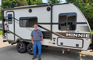 couple sitting outside of their RV beside a lake