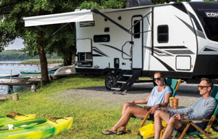 couple sitting outside of their RV beside a lake