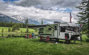 RV parked in a field with mountains in the background.