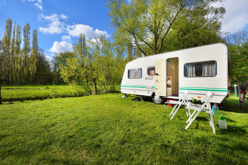 White RV trailer on grassy pasture surrounded by trees in summer