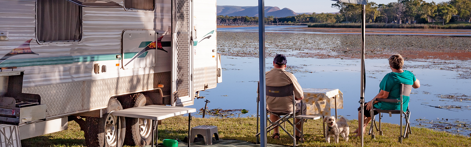 RV parked near a body of water with people gathered by a table