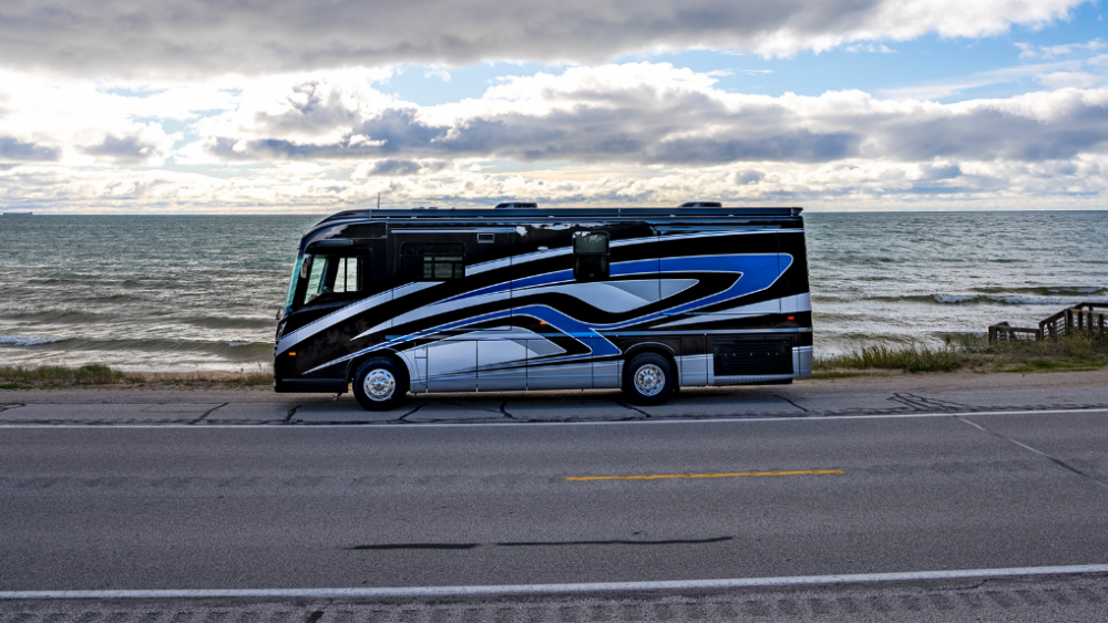 A Winnebago Journey parked by the side of a road by the ocean.