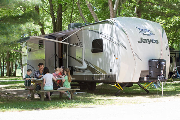 Family sitting at a picnic table outside their RV. Full view of RV.